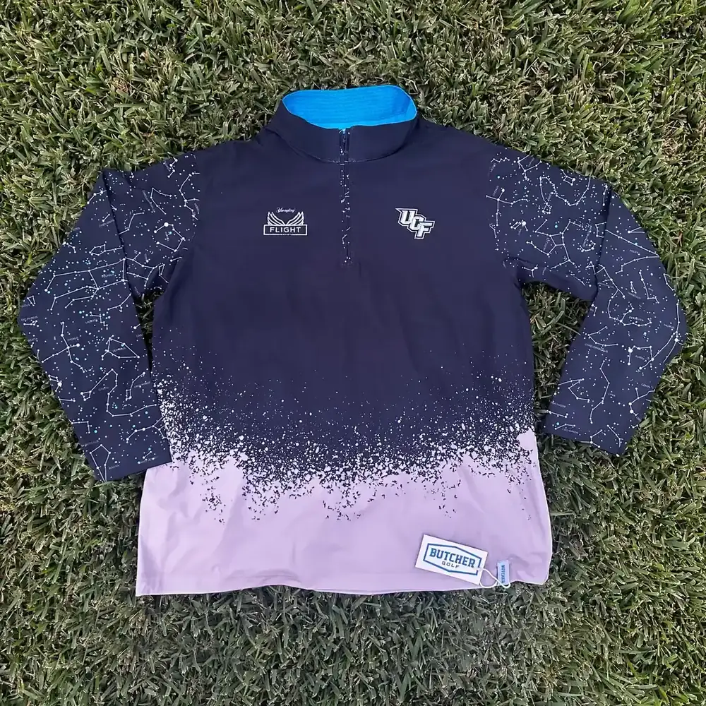 Custom UCF and Yuengling Flight quarter-zip with constellation print and fade, laid flat on grass.