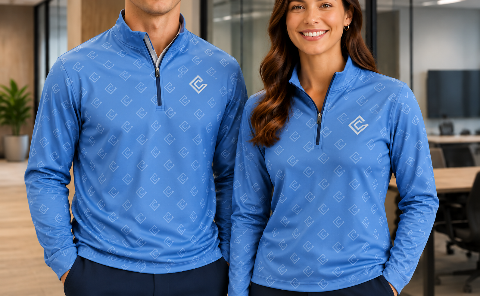 Two colleagues wearing matching custom blue quarter-zips with an all-over brand pattern and chest logo, in an office setting.